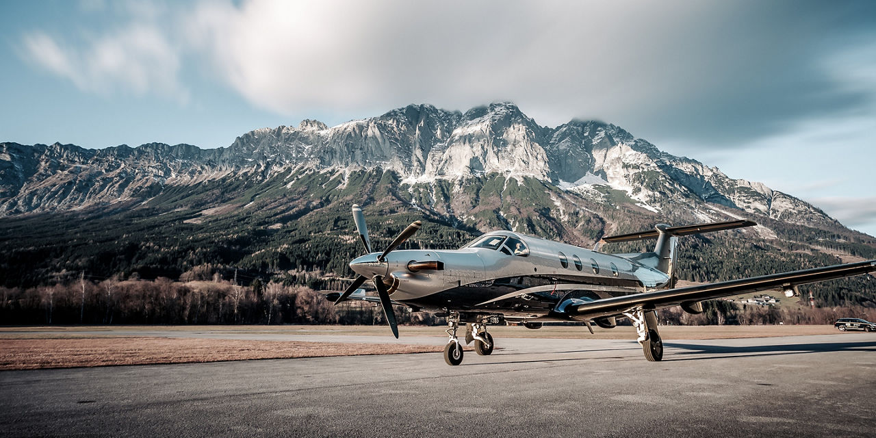 Polished aircraft positioned on tarmac with dramatic rocky peaks behind, combining aviation engineering with rugged natural landscape.