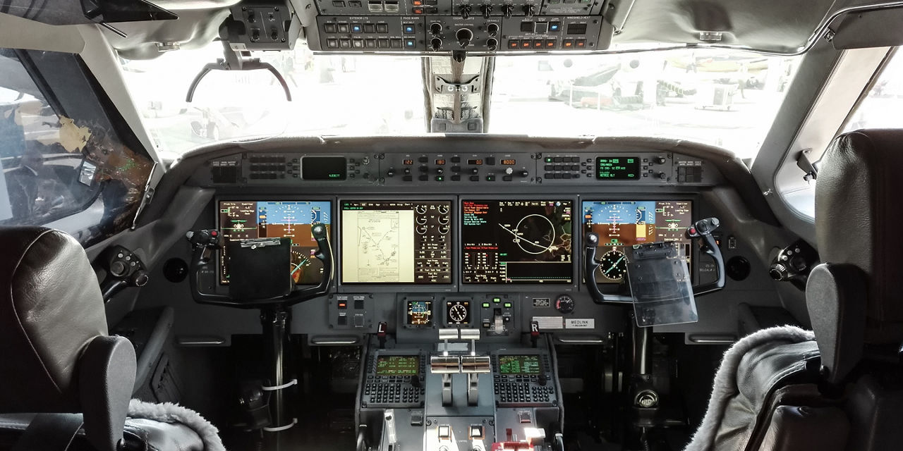Wide cockpit view featuring active screens, control panels and overhead switches, showcasing modern avionics and navigation systems.
