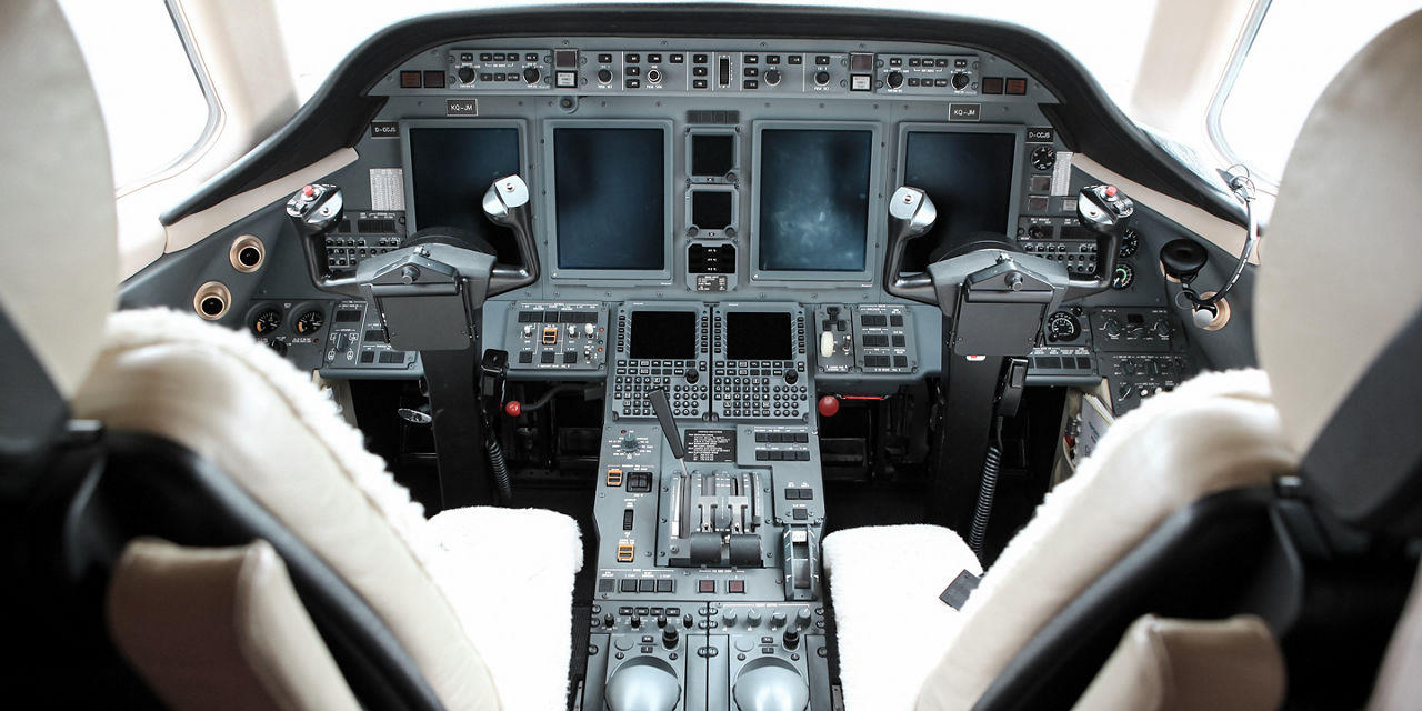 Front-facing cockpit view with control columns, multiple blank screens and central throttle console, highlighting flight control layout and instrument precision.