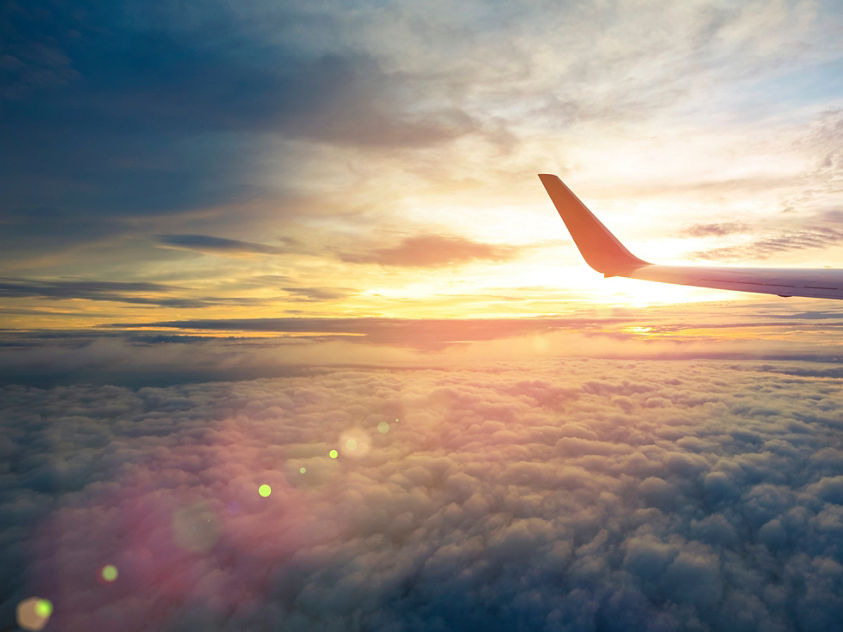 Wing of an airplane flying above the sunriseclouds and flare effect