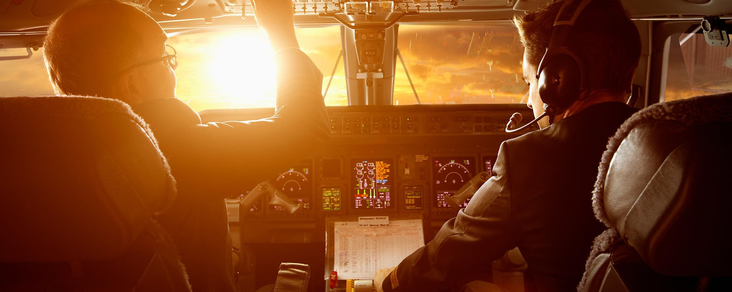  Two pilots in an airplane cockpit, with a vibrant sunset illuminating the scene through the windows.