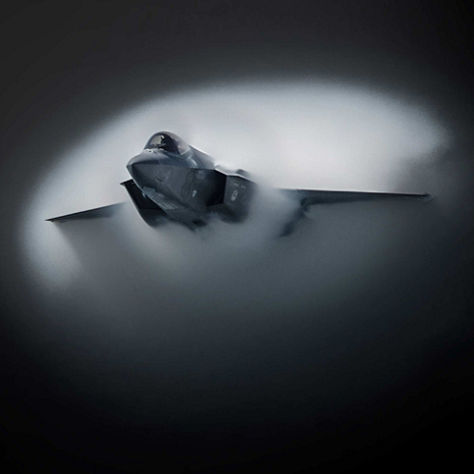 Advanced fighter aircraft cutting through condensed air, forming a circular vapor cloud during high-speed maneuvering.