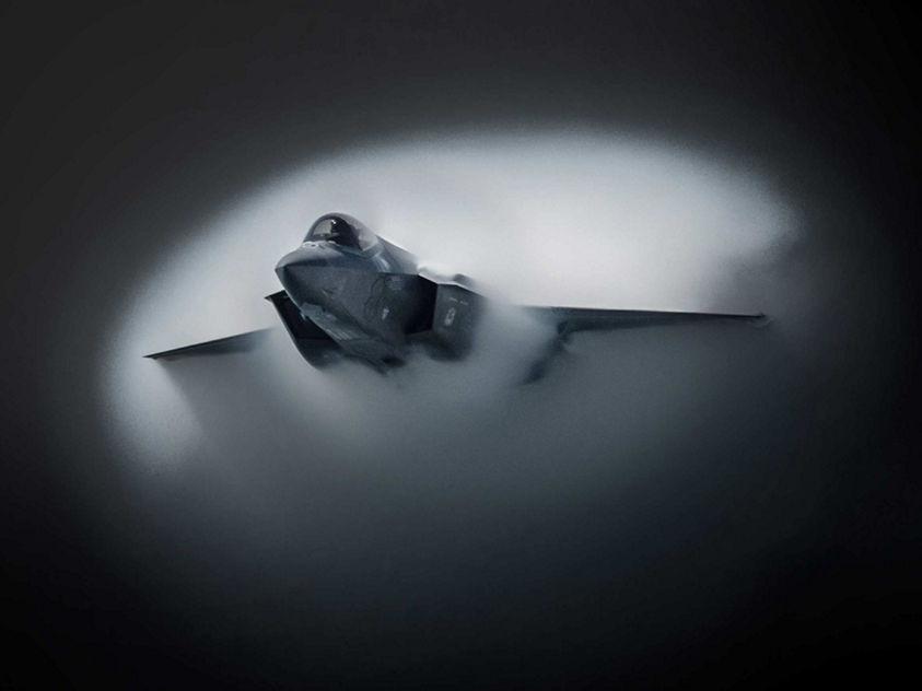 Advanced fighter aircraft cutting through condensed air, forming a circular vapor cloud during high-speed maneuvering.
