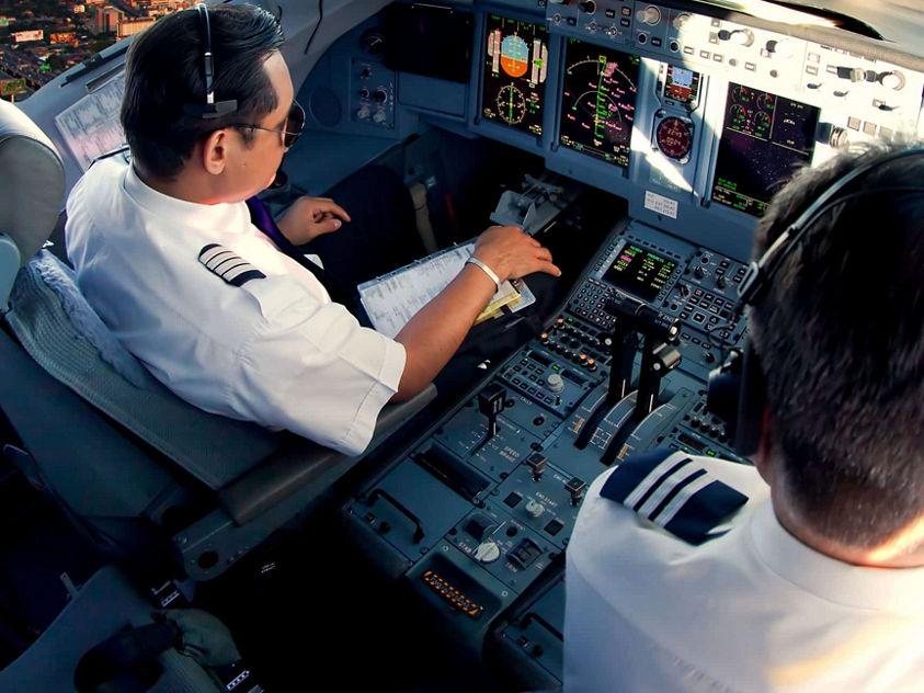 Two pilots are seated in the cockpit of an airplane, surrounded by an array of controls and instruments