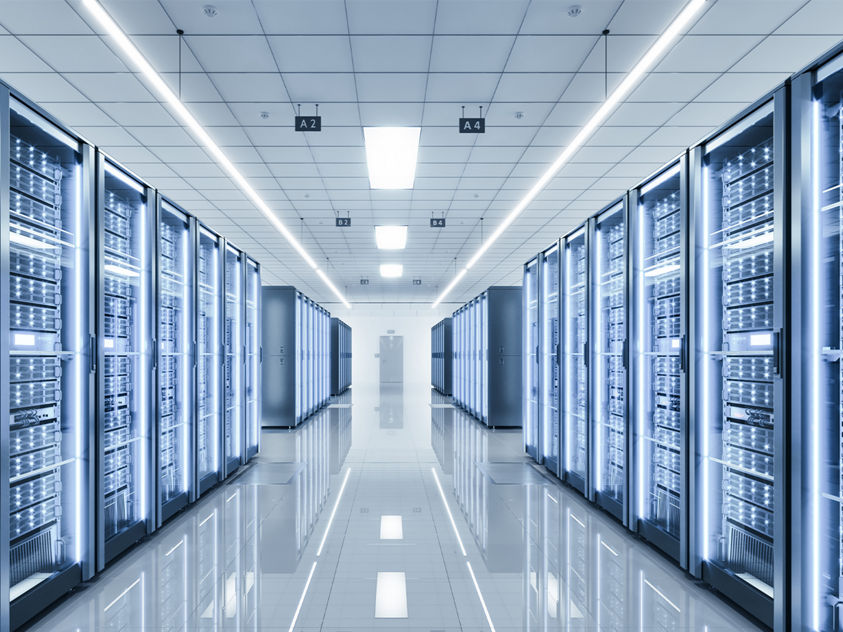 A brightly lit data center hallway lined with tall server racks glowing with cool blue lights, reflecting across a polished floor to emphasize modern, high‑performance computing infrastructure.