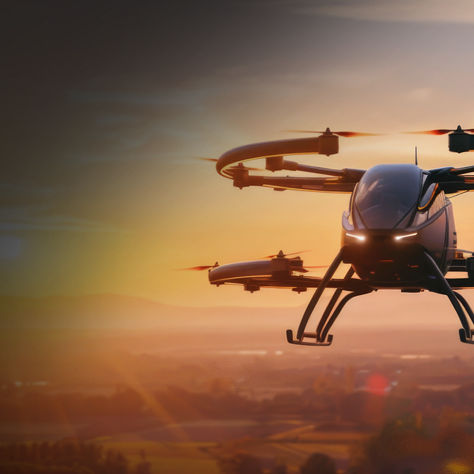 A multi-rotor drone captured mid-flight during sunset, with warm lighting and a scenic backdrop of fields, trees, and hills.