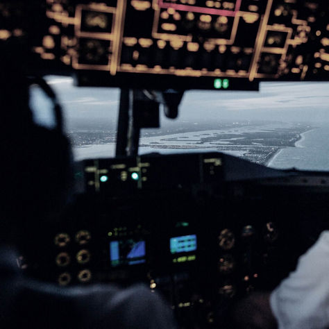 A cockpit view of two pilots guiding an aircraft along the coastline during approach, with flight instruments illuminated and a detailed shoreline visible through the windshield. Ideal for aviation safety, navigation technology, and flight operations content.