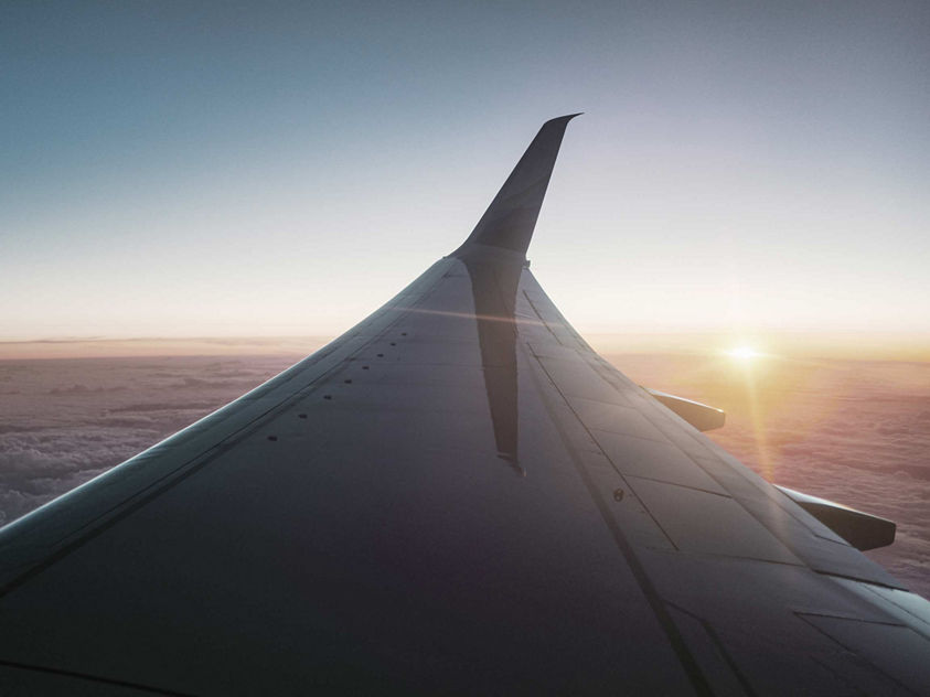 View along a wingtip as sunlight breaks over a wide expanse of clouds during cruise.