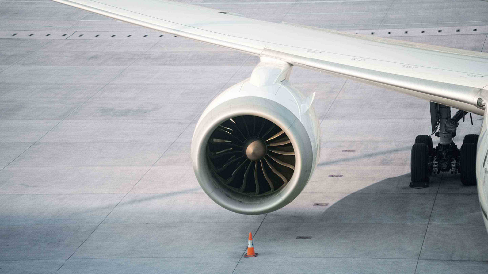 Close-up of a turbofan engine mounted under a wing with safety cone positioned on the apron.