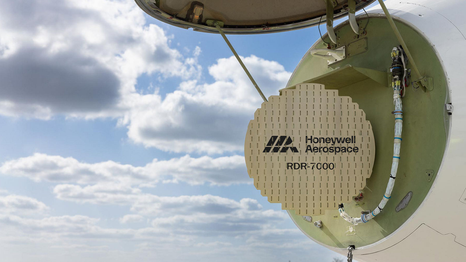 An aircraft’s nose compartment is open, revealing the Honeywell Aerospace RDR‑7000 radar system against a bright sky. The image highlights advanced radar technology and aircraft maintenance access.