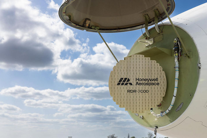 An aircraft’s nose compartment is open, revealing the Honeywell Aerospace RDR‑7000 radar system against a bright sky. The image highlights advanced radar technology and aircraft maintenance access.