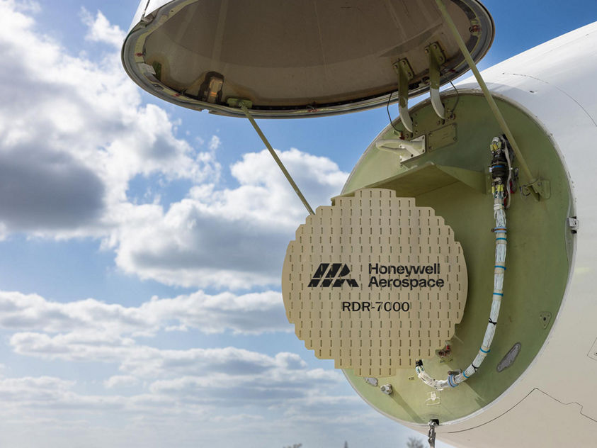 An aircraft’s nose compartment is open, revealing the Honeywell Aerospace RDR‑7000 radar system against a bright sky. The image highlights advanced radar technology and aircraft maintenance access.