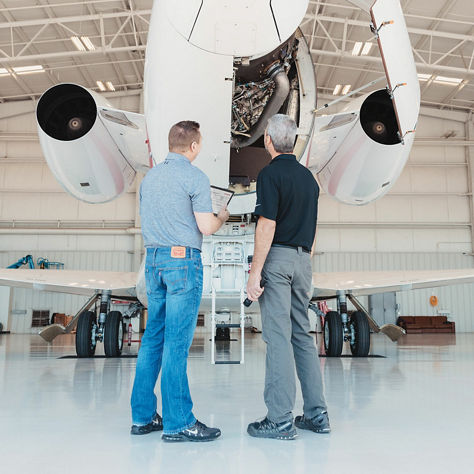 image of two men examine the engine of a private jet while standing in front of it.