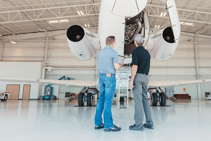 image of two men examine the engine of a private jet while standing in front of it.