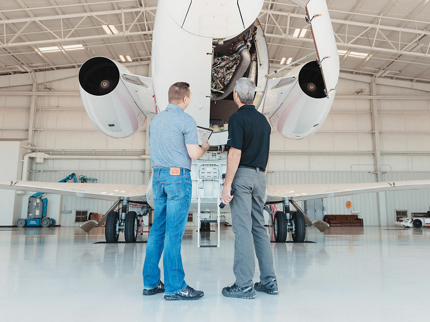 image of two men examine the engine of a private jet while standing in front of it.