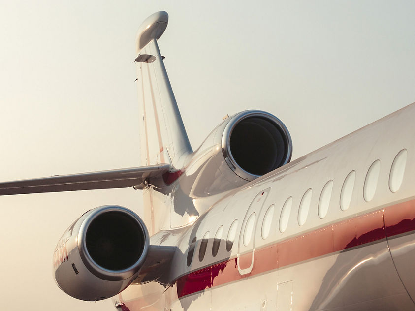 Rear view of a private jet with three engines and red stripe, captured during a scenic sunset or sunrise.