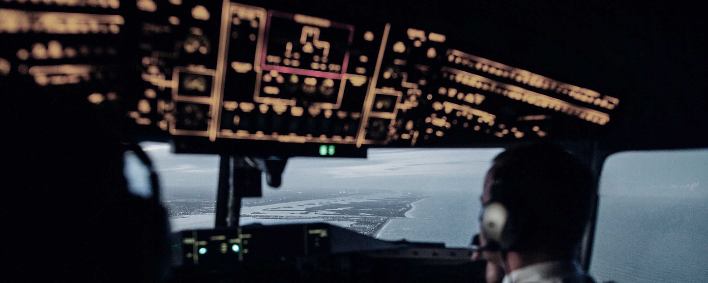 Rear cockpit view of pilots managing instruments while flying along a coastal route.