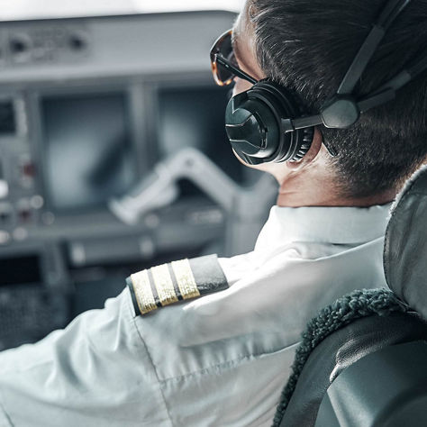 airline pilot wearing a white uniform shirt with epaulets and a headset while seated in the cockpit of an aircraft