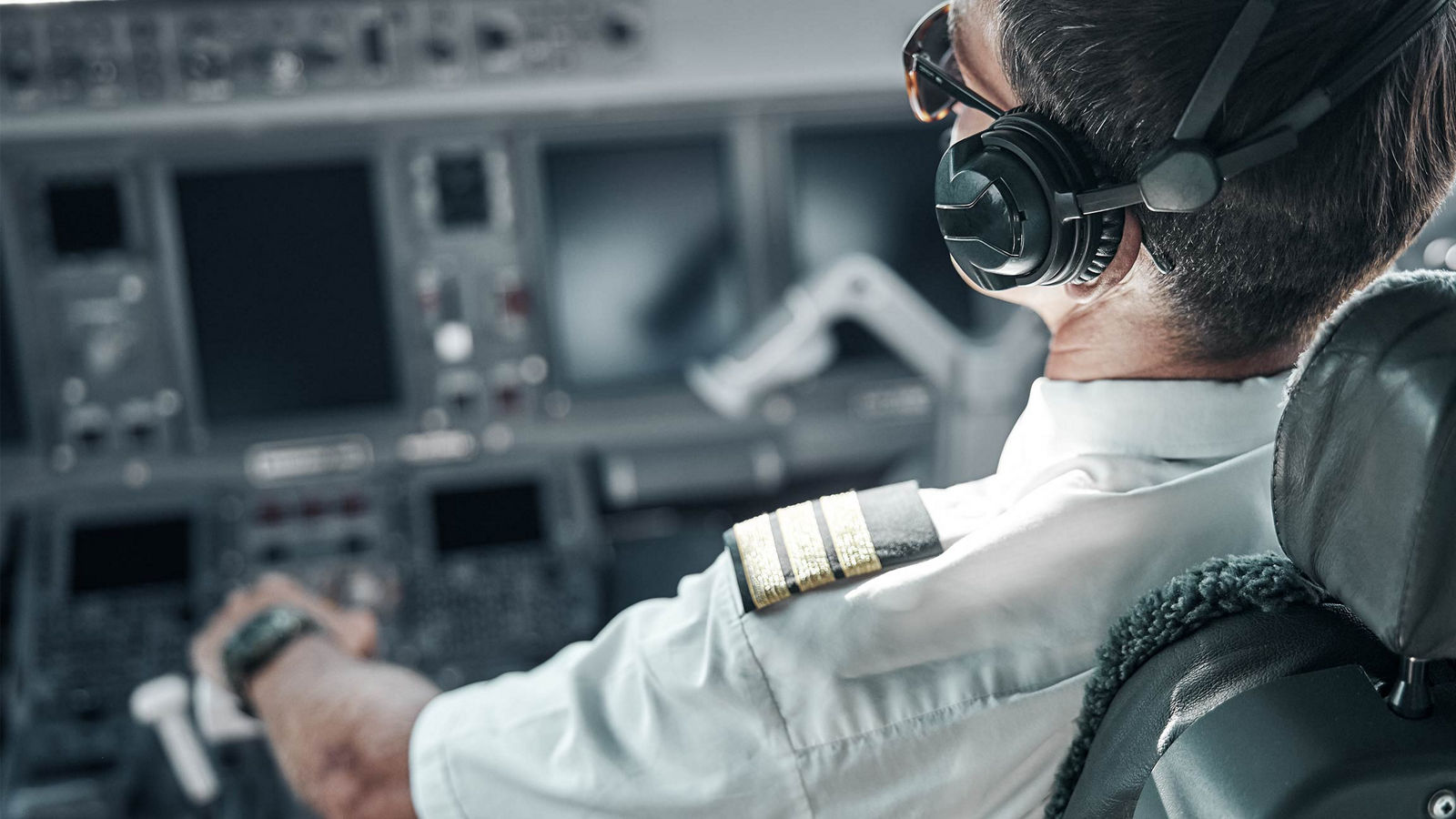 airline pilot wearing a white uniform shirt with epaulets and a headset while seated in the cockpit of an aircraft