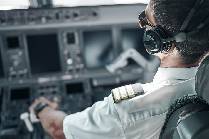 airline pilot wearing a white uniform shirt with epaulets and a headset while seated in the cockpit of an aircraft