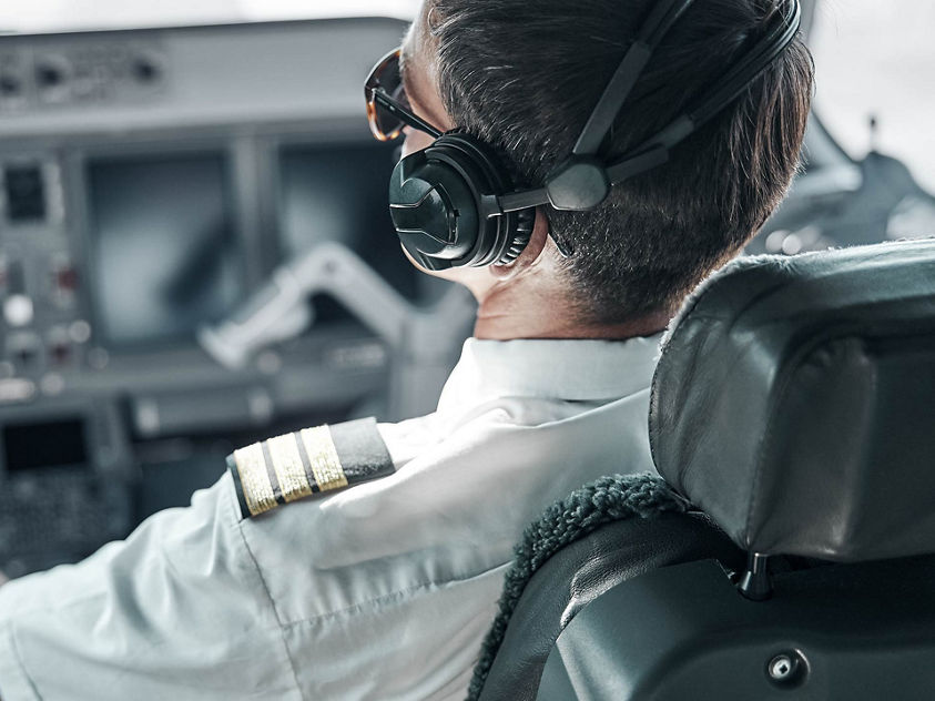 airline pilot wearing a white uniform shirt with epaulets and a headset while seated in the cockpit of an aircraft
