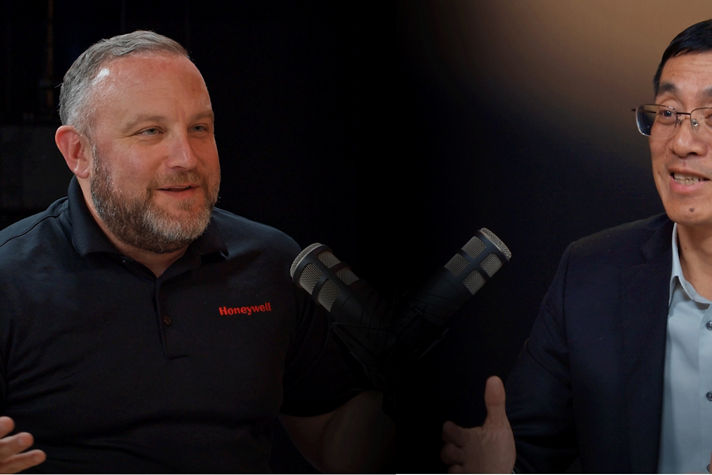 Two individuals discuss industry topics in a formal setting, featuring a Honeywell-branded participant and microphones.