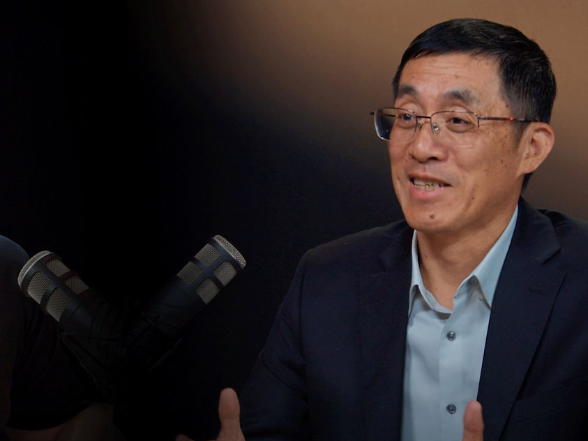 Two individuals discuss industry topics in a formal setting, featuring a Honeywell-branded participant and microphones.