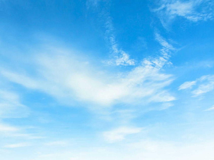 Bright blue sky filled with scattered, wispy white clouds stretching across a clear daytime horizon
