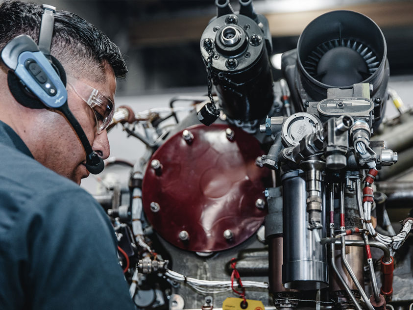 a technician wearing safety glasses and headphones while performing maintenance on a complex jet engine