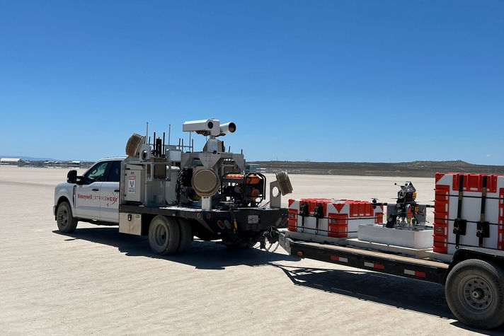 A Honeywell-branded truck equipped with scientific instruments and trailer containers in a wide-open field setting.