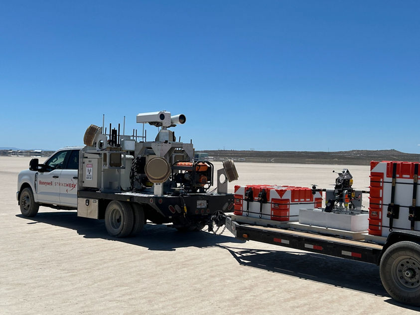 A Honeywell-branded truck equipped with scientific instruments and trailer containers in a wide-open field setting.