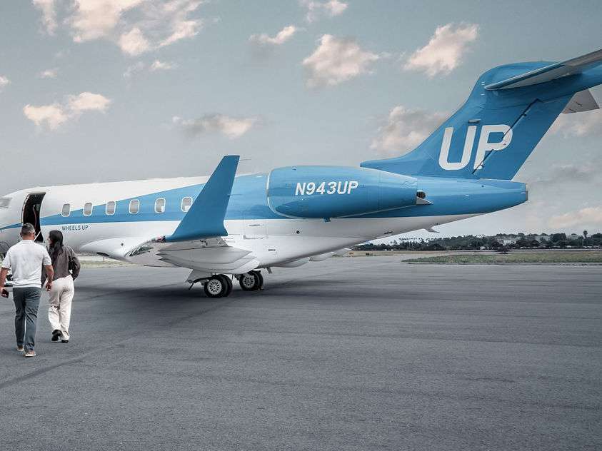 passengers walking toward a blue-and-white Bombardier Challenger 300 private jet operated by Wheels Up