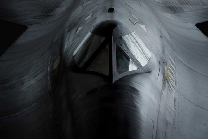 Dramatic frontal view of a military aircraft emphasizing cockpit geometry, metallic surfaces, and stealth-oriented design.