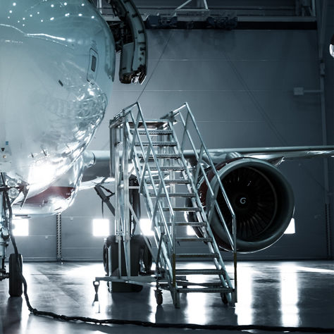 Front view of a commercial aircraft inside a hangar while a technician performs inspection near the landing gear with access equipment nearby
