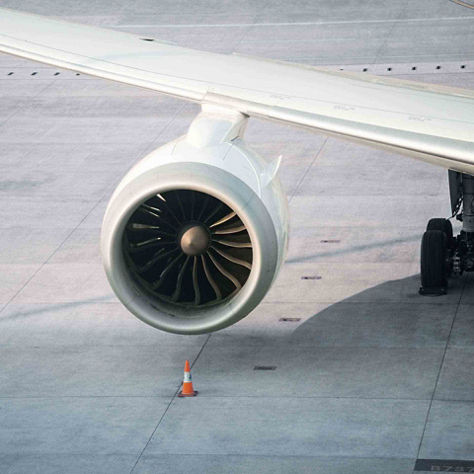 Close-up of a turbofan engine mounted under a wing with safety cone positioned on the apron.