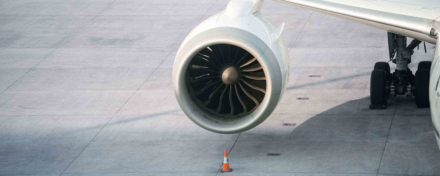 Close-up of a turbofan engine mounted under a wing with safety cone positioned on the apron.