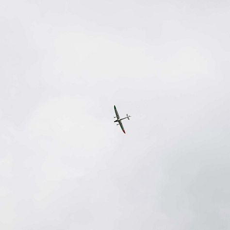 A small glider or UAV is captured as a tiny silhouette flying in a wide overcast grey sky, emphasized by the vast empty sky around it. The minimalist composition suggests Honeywell's unmanned systems and UAV navigation technology in low-signature environments.