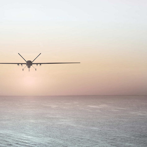 Long-wing unmanned aerial vehicle flying above calm sea at sunrise or sunset.
