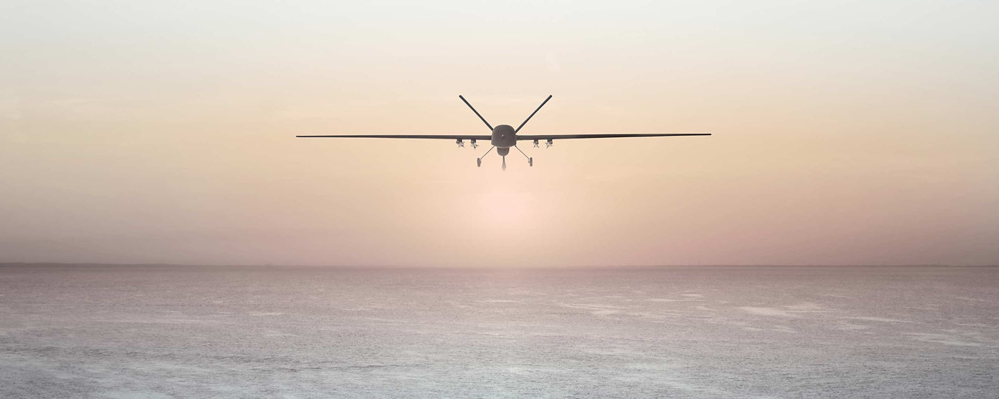 Long-wing unmanned aerial vehicle flying above calm sea at sunrise or sunset.