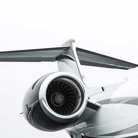 Clean close-up of a business jet's tail section showing one rear-mounted turbofan engine and the horizontal stabilizer, photographed on a ramp against a white overcast sky. This image represents Honeywell's business jet engine, APU, and tail systems technology.