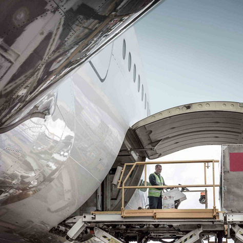 A cargo handler on a scissor lift loads freight through the open belly cargo door of a large commercial aircraft on an airport ramp, under the distinctive curved fuselage. This image represents Honeywell's aircraft cargo management and ground handling solutions.